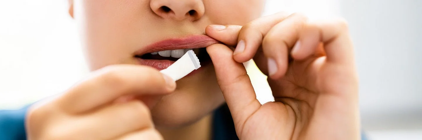 Eine junge Person steckt sich ein weißes Snus-Beutelchen unter die Oberlippe.