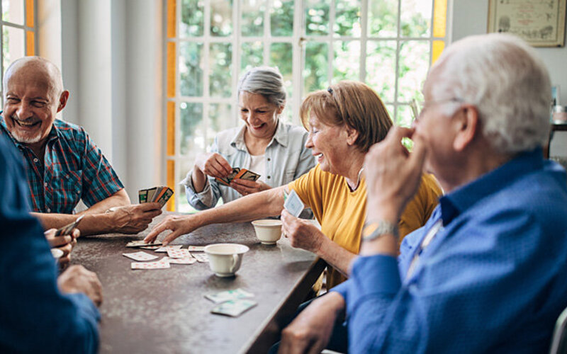 Mehrere Senioren sitzen in einer Senioren-WG-Küche zusammen und spielen Karten.