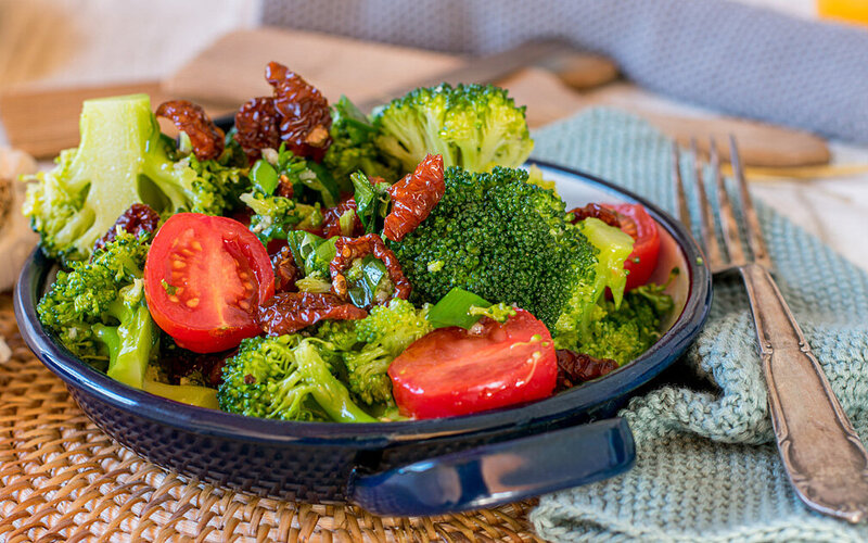 Brokkoli-Tomaten-Salat steht in einer Keramikschale auf einem Tisch.