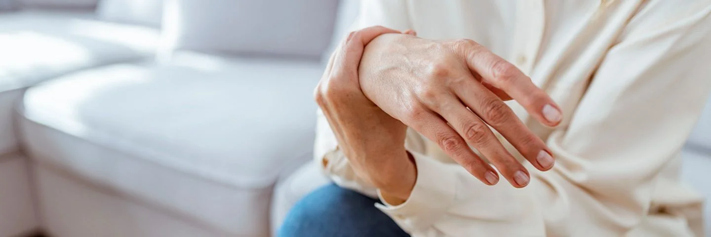 Frau leidet durch ihre Fibromyalgie unter schmerzenden Gelenken und massiert ihre Hand.