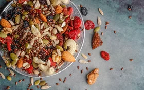 Eine kleine Glasschale gefüllt mit unterschiedlichen Nüssen, Mandeln, Kürbis- und Sonnenblumenkernen, Leinsamen sowie Rosinen und getrockneten Cranberries.