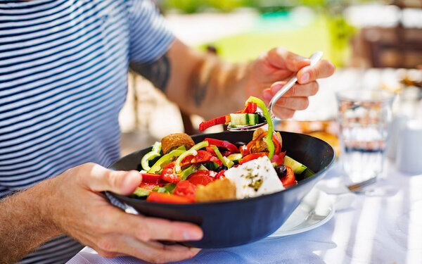 Frischer Salat mit Paprika, Gurken, Oliven und Feta in einer dunkelblauen Schüssel.