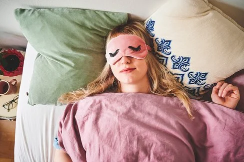 Eine junge Frau liegt im Bett und trägt eine Schlafmaske.