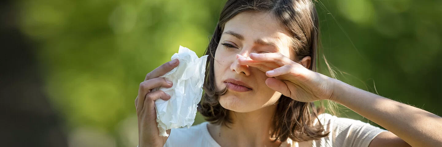 Frau reibt sich mit einer Hand die juckenden Augen, in der anderen Hand hält sie ein Papiertaschentusch.