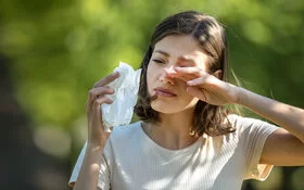 Frau reibt sich mit einer Hand die juckenden Augen, in der anderen Hand hält sie ein Papiertaschentusch.