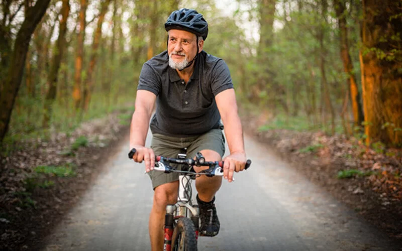 Älterer Mann ist mit dem Rad unterwegs, um durch die regelmäßige Bewegung einer Kniearthrose vorzubeugen.