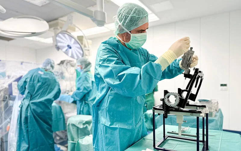 In einem Operationssaal der Uniklinik Köln überprüft ein Arzt in OP-Schutzkleidung vor der Operation die Funktionsfähigkeit des stereotaktischen Rahmens.