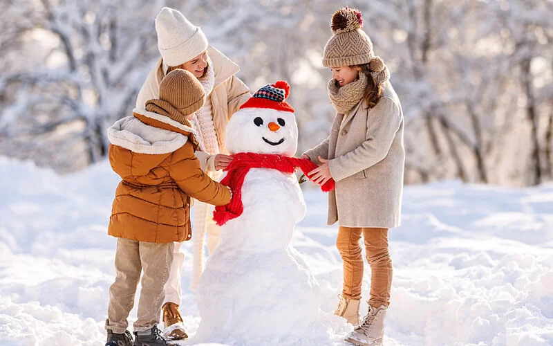 Mutter und zwei Kinder bauen einen Schneemann.