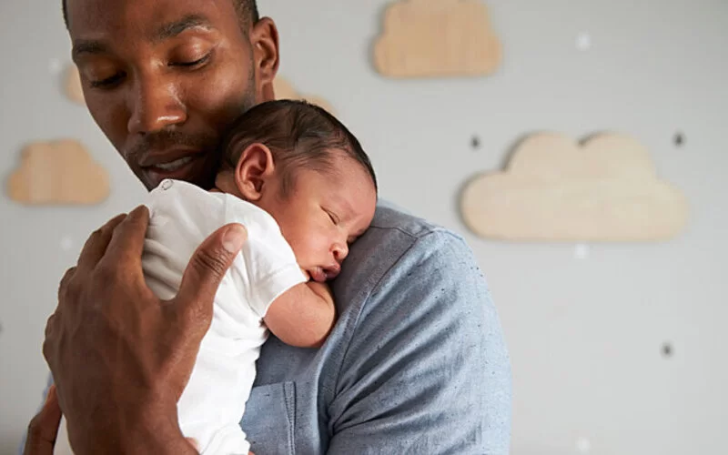 Ein Vater mit Keuchhusten-Impfung hält ein Neugeborenes auf dem Arm.