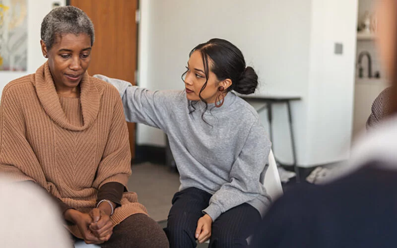 Zwei Frauen bei einer Therapiegruppe zur Trauerbewältigung schenken sich gegenseitig Trost.