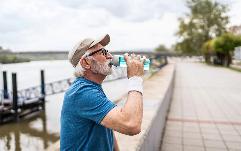Ein älterer Mann trinkt nach dem Joggen Wasser aus einer Trinkflasche.