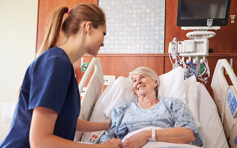 Eine Krankenschwester spricht mit einer älteren Patientin in einem Krankenbett über die bevorstehende Operation.