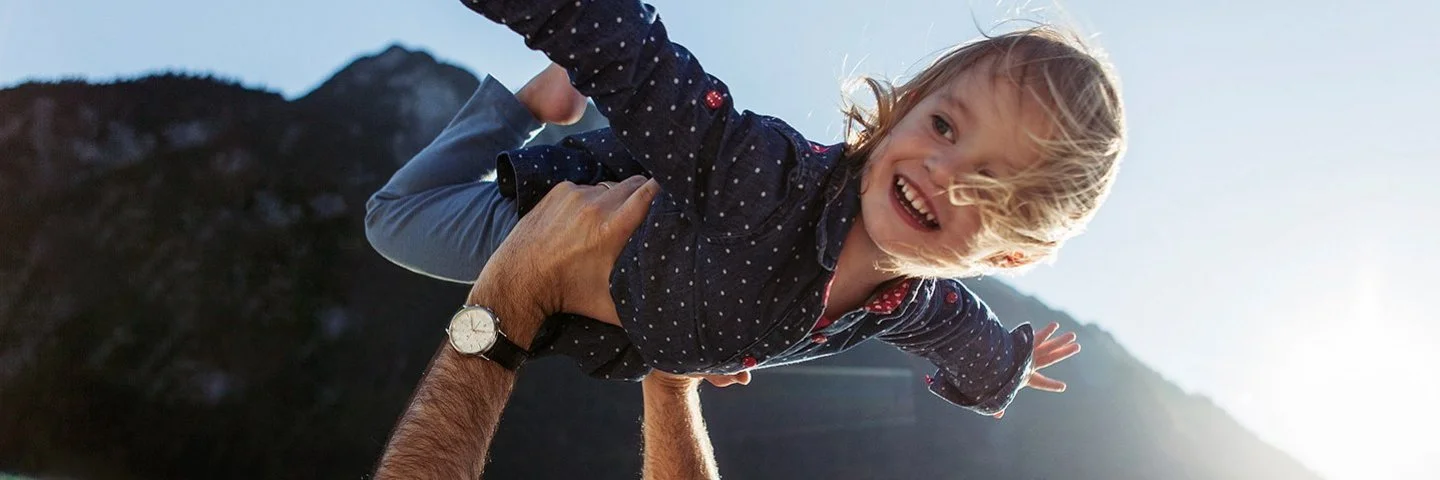 Ein glückliches kleines Mädchen mit ausgebreiteten Armen, das von seinem Vater getragen wird.