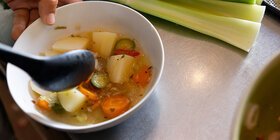 Eine Hand hält eine Schale mit einer Brühe mit Gemüse. Bei der richtigen Ernährung unterstützt Sie die AOK.