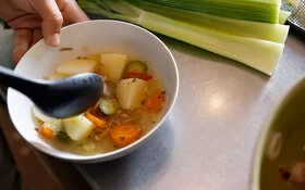 Eine Hand hält eine Schale mit einer Brühe mit Gemüse. Bei der richtigen Ernährung unterstützt Sie die AOK. 