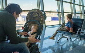 Ein Vater ist mit einem Baby im Kinderwagen und einem älteren Kind in einem Flughafen.