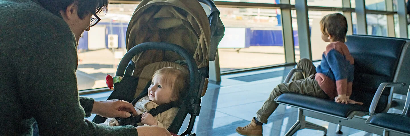 Ein Vater ist mit einem Baby im Kinderwagen und einem älteren Kind in einem Flughafen.