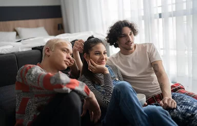Zwei männliche und eine weibliche Person sitzen zusammen auf dem Fußboden und sehen fern.