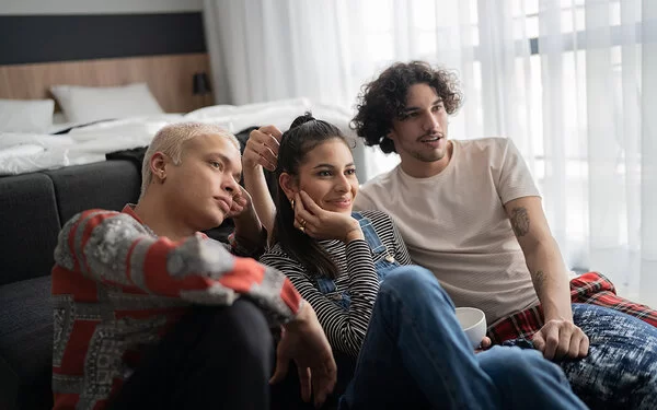 Zwei männliche und eine weibliche Person sitzen zusammen auf dem Fußboden und sehen fern.
