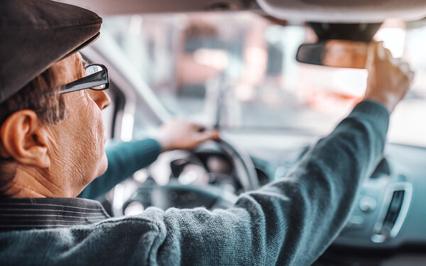 Ein älterer Autofahrer justiert den Rückspiegel seines Autos.