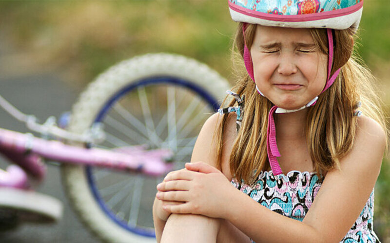 Ein Mädchen sitzt auf dem Boden und weint nach einem Fahrradunfall.