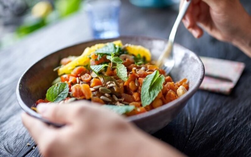 Ein vegetarischer Salat mit Kichererbsen, Möhren und Sonnenblumenkernen in einer grauen Keramikschale, garniert mit Minzblättern. 