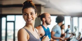 Eine junge Frau steht in einem Fitness-Studio auf einem Laufband und lacht in die Kamera