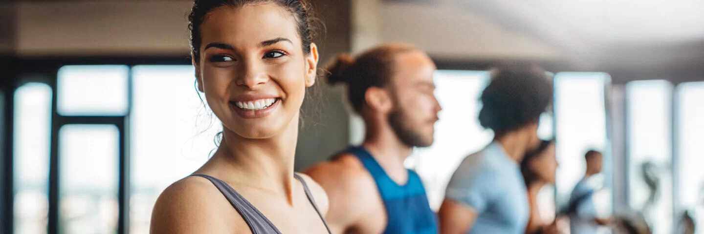 Eine junge Frau steht in einem Fitness-Studio auf einem Laufband und lacht in die Kamera