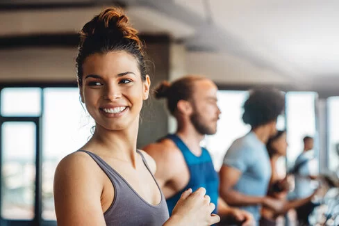 Eine junge Frau steht in einem Fitness-Studio auf einem Laufband und lacht in die Kamera