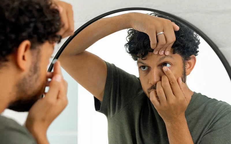 Ein junger Mann setzt sich vor einem Spiegel eine Kontaktlinse ein.