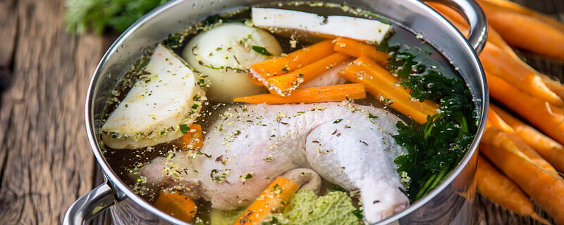 Viele frische Zutaten in einem Kochtopf für eine gesunde Hühnerbrühe.