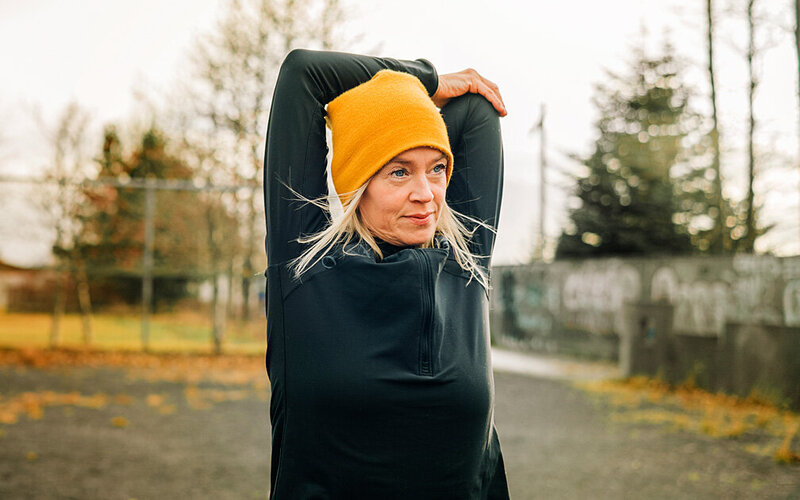 Eine Frau dehnt sich die Arme vor dem Laufen – die Bewegung hilft ihr beim Stressabbau und Rauchstopp.