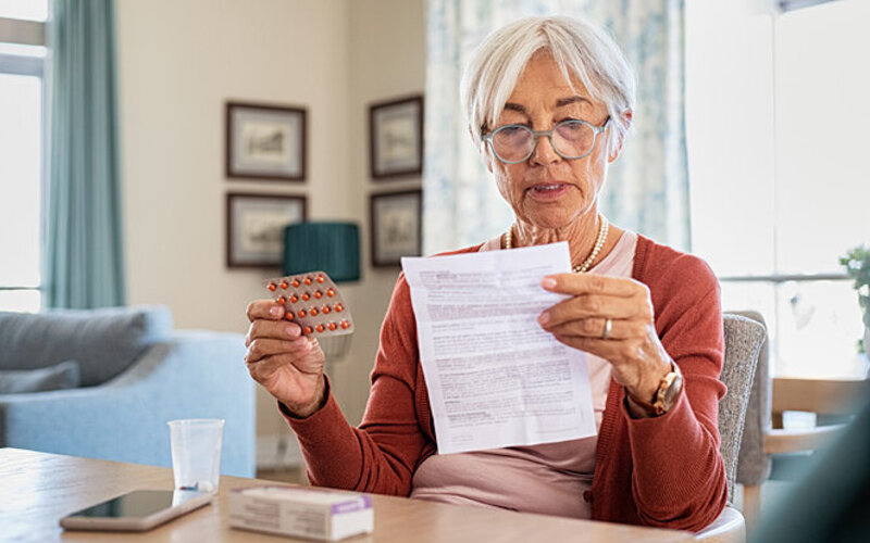 Eine ältere Dame liest sich den Beipackzettel von einem Medikament durch, um herauszufinden, ob Sie die Tabletten nüchtern einnehmen muss.