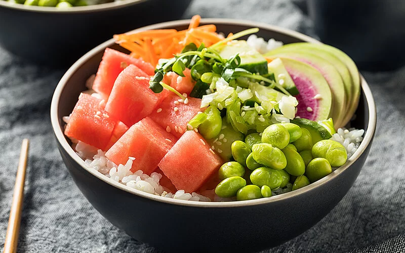 Eine selbstgemachte Bowl mit Reis, Edamame, Wassermelone und Kräutern in einem Schüsselchen.