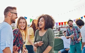 Mehrere junge Menschen stehen in kleinen Grüppchen oder sitzen allein herum und feiern eine Dachparty.