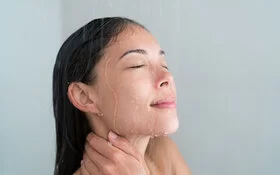 Eine junge Frau lässt unter der Dusche Wasser über ihr Gesicht laufen.