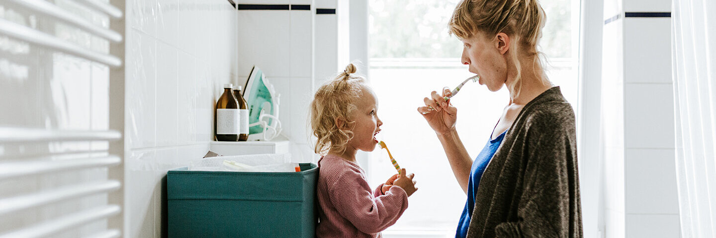 Eine junge Mutter putzt mit ihrem Kind Zähne
