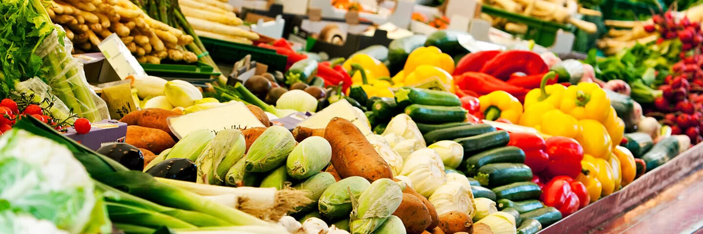 Frisches Gemüse und Obst wird auf einem Marktstand zum Verkauf angeboten. Darunter auch präbiotische Lebensmittel wie Spargel und Süßkartoffeln.