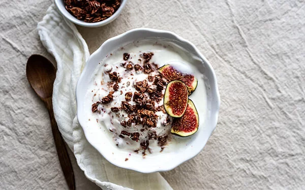 Eine Schale Joghurt mit Müsli und Feigen stehen auf einem Tisch.