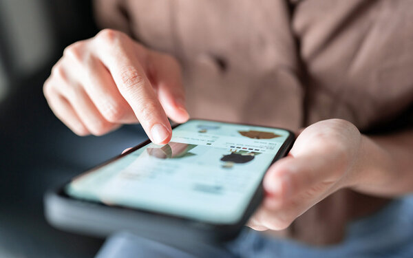 Im Vordergrund ein Smartphone, das Kleiderauswahl in einem Onlineshop zeigt. Ein Finger wischt über die Angebote.
