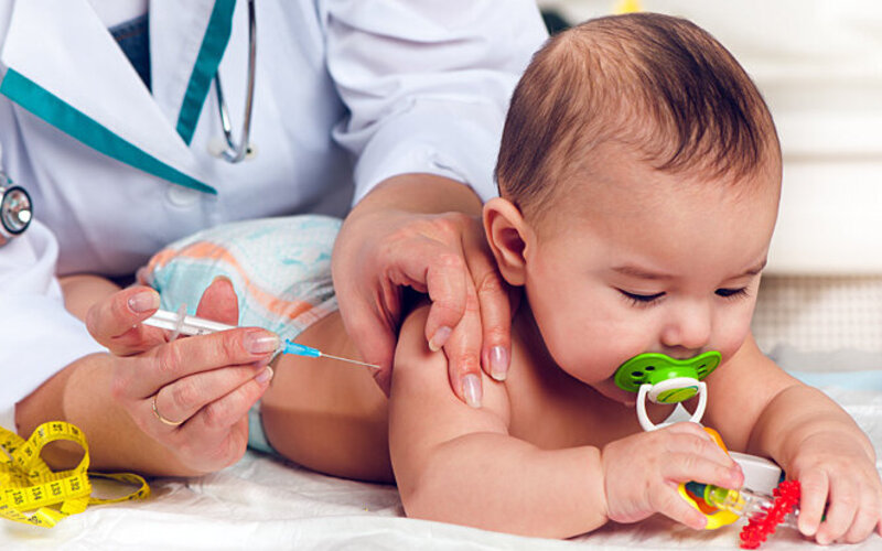 Eine Krankenschwester setzt eine Spritze mit Impfstoff am Oberarm eines Babys an.