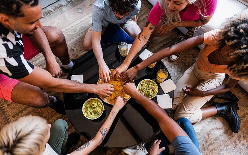 Mehrere Menschen sitzen um einen Tisch herum und greifen in eine Schüssel mit Nachos.