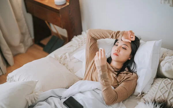 Eine Frau liegt im Bett und hält ein Fieberthermometer in der Hand.