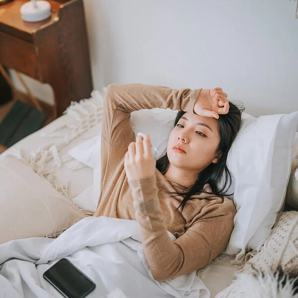 Eine Frau liegt im Bett und hält ein Fieberthermometer in der Hand.