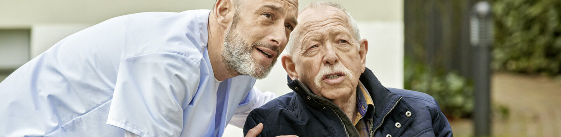 Ein Pfleger begleitet einen älteren Herrn im Rollstuhl. Mit der AOK Pflegezusatzversicherung sind Pflegebedürftige über das Gesetz hinaus abgesichert.