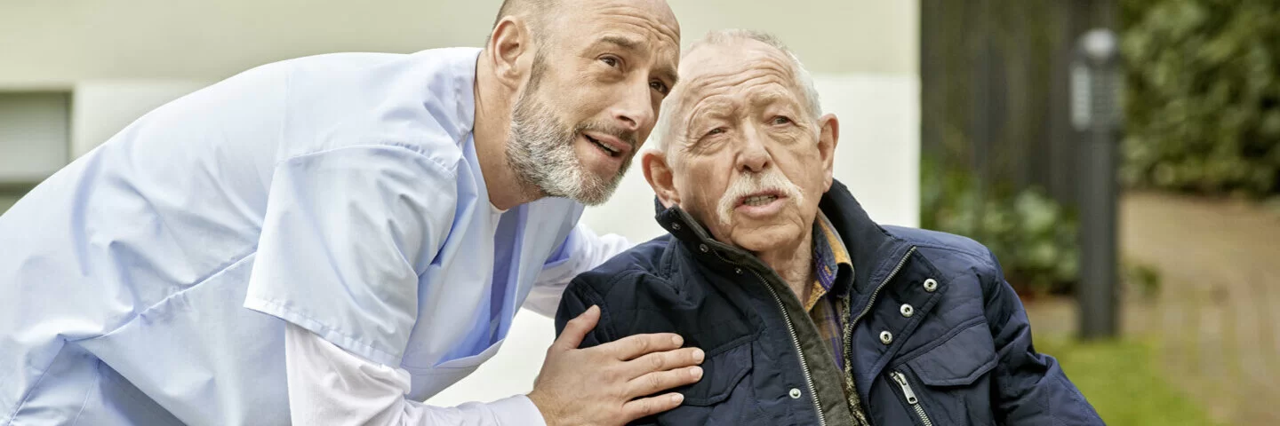Ein Pfleger begleitet einen älteren Herrn im Rollstuhl. Mit der AOK Pflegezusatzversicherung sind Pflegebedürftige über das Gesetz hinaus abgesichert.