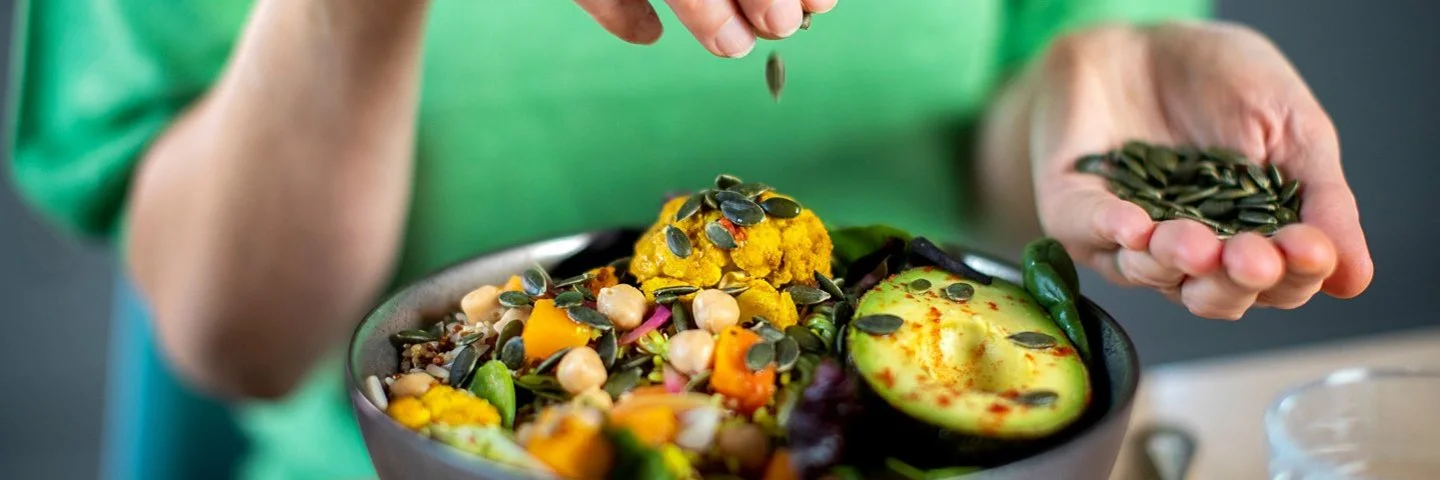 Frau streut Kürbiskerne über eine vegane Bowl.