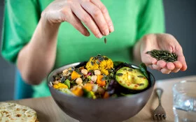 Frau streut Kürbiskerne über eine vegane Bowl.