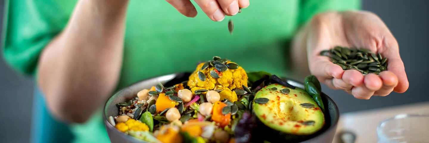 Frau streut Kürbiskerne über eine vegane Bowl.