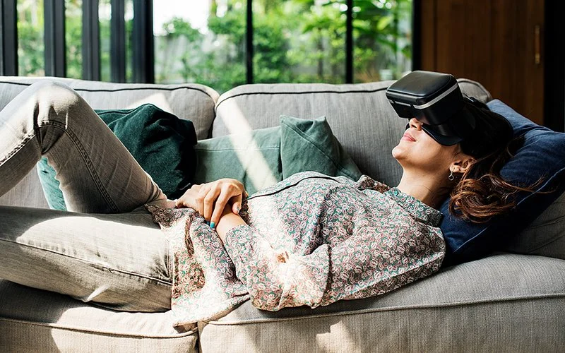 Eine Frau liegt mit einer VR-Brille entspannt auf dem Sofa.